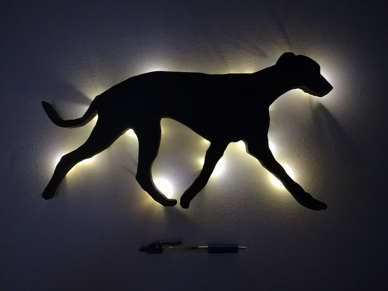 May include: A black silhouette of a dog running, lit up with white lights, mounted on a white wall.