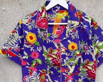 May include: A purple short-sleeved shirt with a white collar and button closure. The shirt features a colorful floral and bird print.
