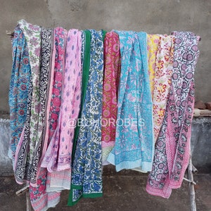 May include: A collection of eight colourful cotton scarves with floral patterns. The scarves are hanging on a wooden rack.
