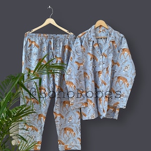 Puede incluir: Un conjunto de pijama azul con estampado de zorro, ciervo y búho. El conjunto incluye una camisa de manga larga con cuello y un pantalón.