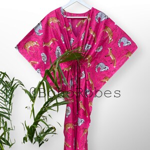 May include: A pink kaftan with a print of various woodland animals, including deer, foxes, owls, and raccoons. The kaftan has a V-neck and a tie at the waist.