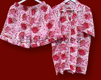 May include: A two-piece pyjama set consisting of a short-sleeved button-down shirt with a collar and a pair of shorts with an elastic waistband. Both pieces feature a pink and white floral pattern with the text @BohoRobes printed across the centre.