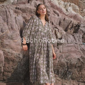 May include: A long, flowing dress with a V-neck and floral pattern in shades of green and pink. The dress has wide sleeves and is worn with sandals. The text "@BohoRobes" is visible on the dress.