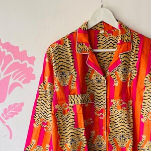May include: A long-sleeved button-up shirt with a pink and orange striped pattern and a tiger print.