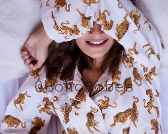 May include: A white pajama top with a brown tiger print. The top has a button-up front and long sleeves. The person is holding a white mug with black coffee.