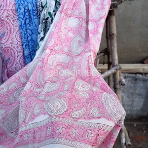 May include: Pink and white paisley patterned fabric with a white border. The fabric is folded and draped over a wooden ladder.