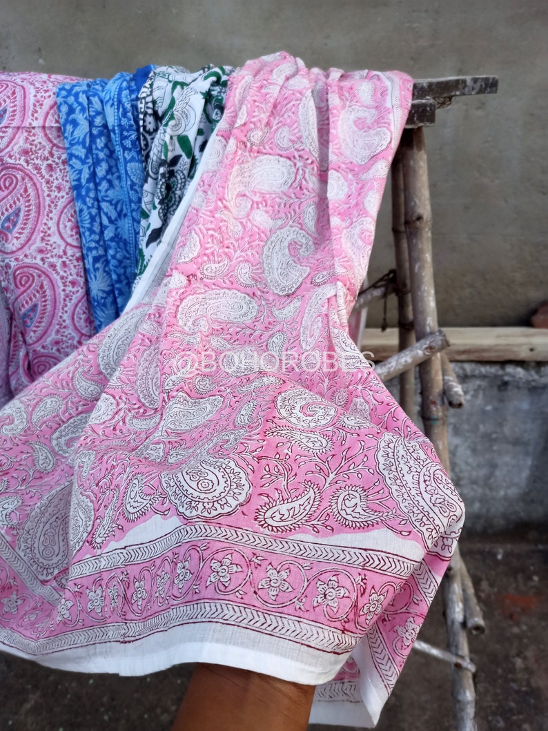 May include: Pink and white paisley patterned fabric with a white border. The fabric is folded and draped over a wooden ladder.