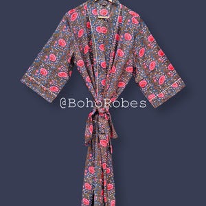 Può includere: Accappatoio con stampa floreale nei toni del blu, rosa e marrone, appeso a una gruccia di legno. L'accappatoio presenta un motivo ripetuto di fiori rosa e foglie marroni su sfondo blu, con bordatura bianca. Il testo "@BohoRobes" è visibile.