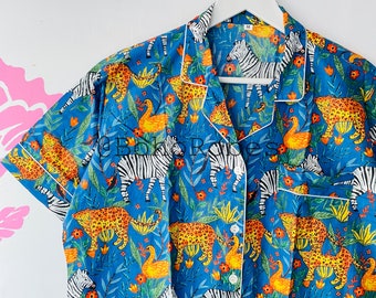 May include: A blue pajama top with a white collar and short sleeves. The top features a colorful print of zebras, leopards, and birds on a blue background.