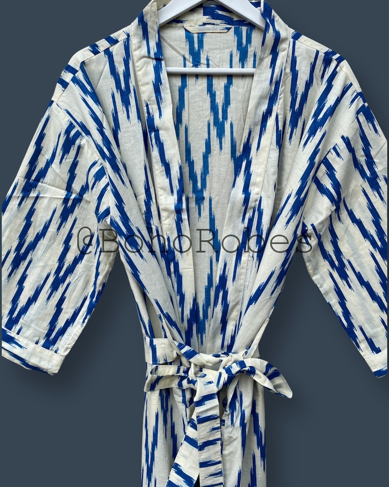 May include: A white cotton robe with a blue ikat pattern. The robe has a tie belt and long sleeves.