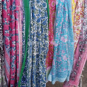 May include: A collection of six colourful cotton saris with floral patterns. The saris are hanging on a clothesline and are ready to be worn.