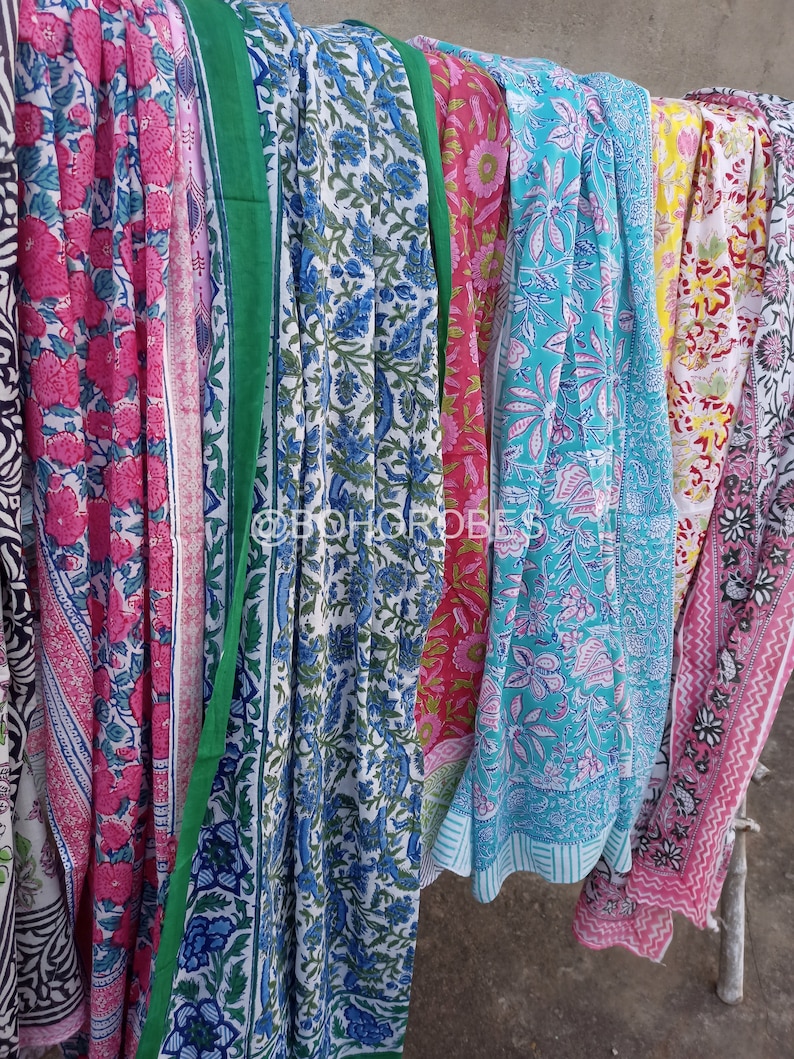 May include: A collection of six colourful cotton saris with floral patterns. The saris are hanging on a clothesline and are ready to be worn.