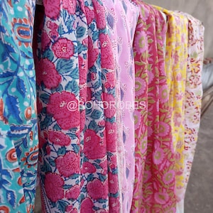 May include: Five colourful fabric scarves with floral patterns. The scarves are hanging on a line and are made of a soft, lightweight material. The scarves are in shades of pink, blue, yellow, and green.