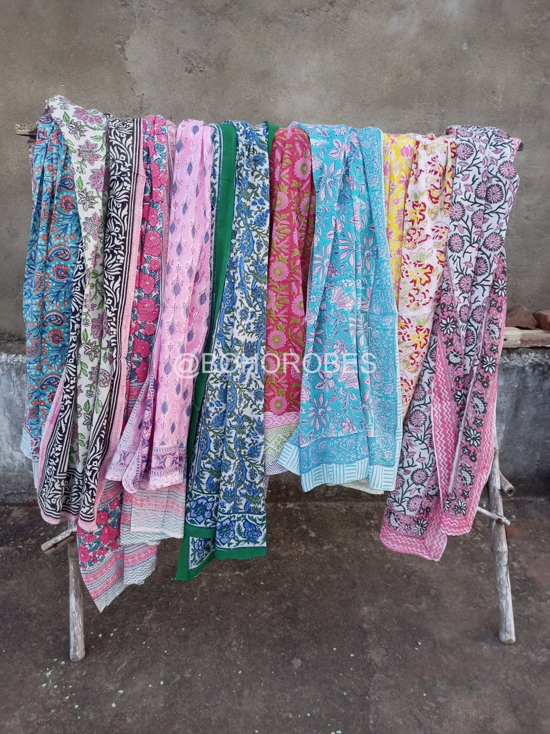 May include: A collection of eight colourful cotton scarves with floral patterns. The scarves are hanging on a wooden rack.