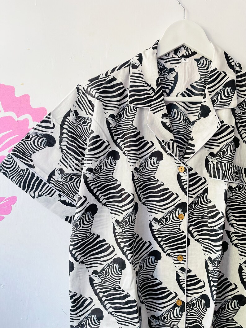 May include: A white button-down shirt with a black and white zebra print. The shirt has a collar and short sleeves.