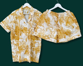 May include: A two-piece pajama set featuring a button-down shirt and shorts. The set is white with a repeating pattern of yellow trees, animals, and foliage. The shirt has short sleeves and a collar. The shorts have a drawstring waist.