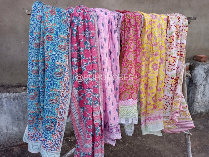 May include: A collection of six colourful cotton scarves with floral patterns hanging on a rack. The scarves are in shades of blue, pink, yellow, and red.