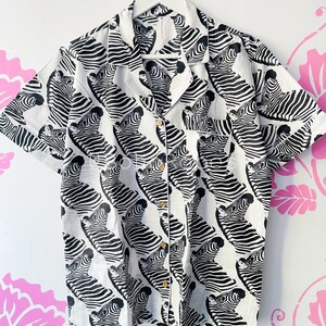 May include: A white short-sleeved button-up shirt with a black and white zebra print.