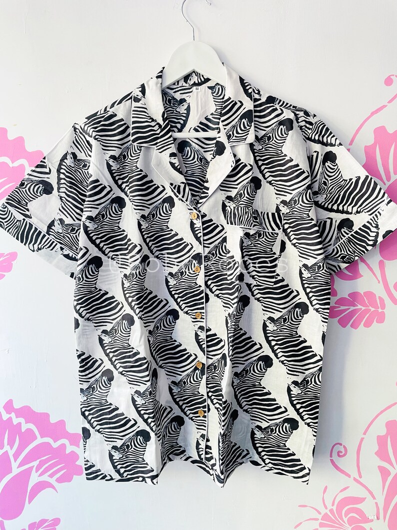 May include: A white short-sleeved button-up shirt with a black and white zebra print.
