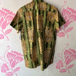 May include: A green and gold short-sleeved button-down shirt with a tiger print.