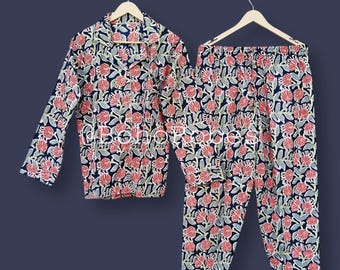Könnte beinhalten: Ein zweiteiliges Pyjama-Set mit floralem Muster. Das Set besteht aus einem langärmeligen Hemd mit Knöpfen und einer passenden Hose. Der Stoff hat einen marineblauen Hintergrund mit einem sich wiederholenden Muster aus rosa Blumen und grünen Blättern.