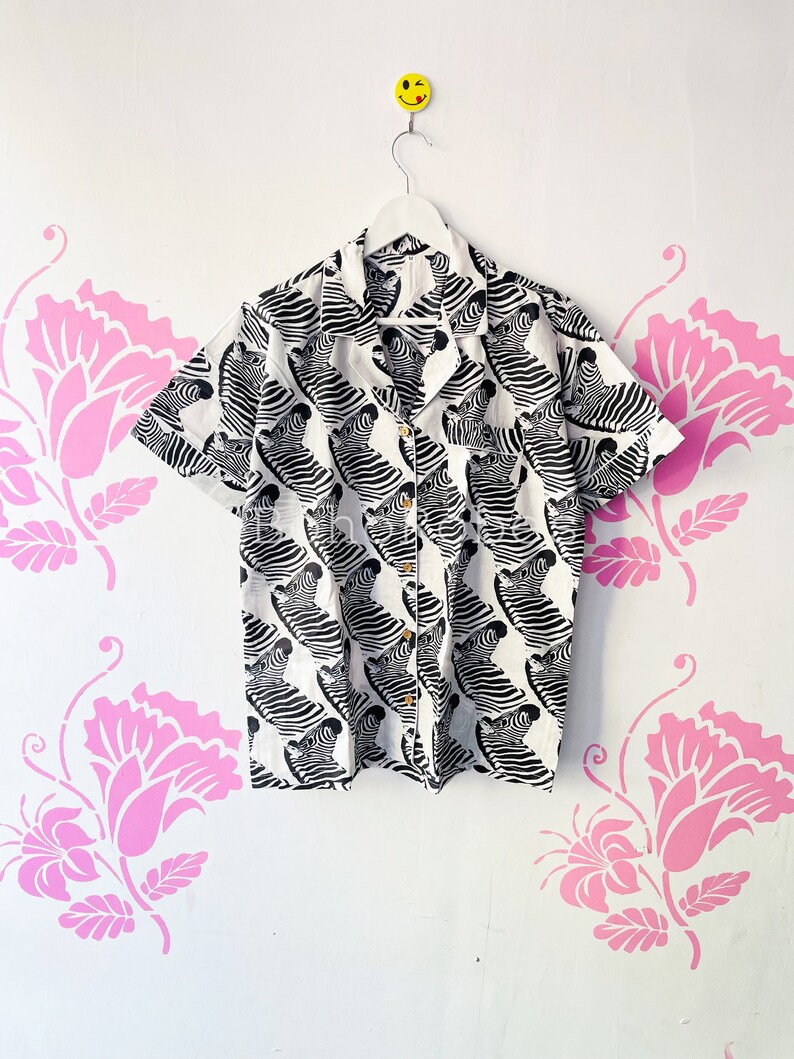 May include: A white short-sleeved button-up shirt with a black and white zebra print.