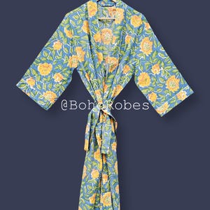Può includere: Un accappatoio floreale blu con fiori gialli e foglie verdi. L'accappatoio ha una cintura abbinata e finiture bianche. Il testo "@BohoRobes" è visibile sull'accappatoio.