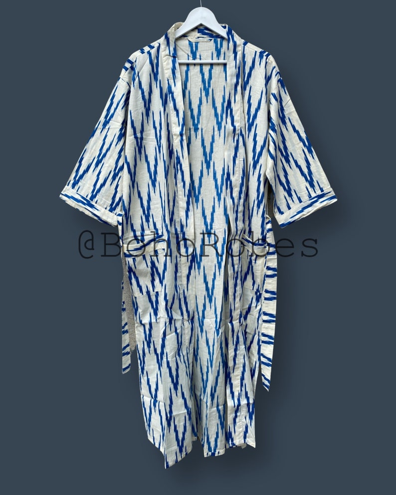 May include: A white and blue patterned robe with a long sleeve and a tie belt. The robe has a chevron pattern in blue on a white background.