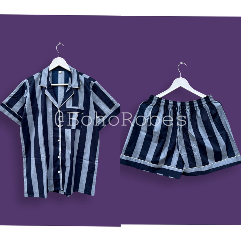 K&ouml;nnte beinhalten: Ein gestreiftes Pyjama-Set mit einem kurz&auml;rmeligen Hemd mit Kn&ouml;pfen und einer passenden Hose. Das Hemd und die Hose sind schwarz und grau mit wei&szlig;en Streifen. Das Set h&auml;ngt an zwei wei&szlig;en Kleiderb&uuml;geln.