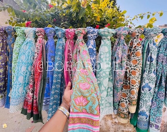 May include: A collection of colorful printed scarves hanging on a wall. The scarves are made of cotton and have a variety of floral and geometric patterns. The scarves are all different lengths and widths.