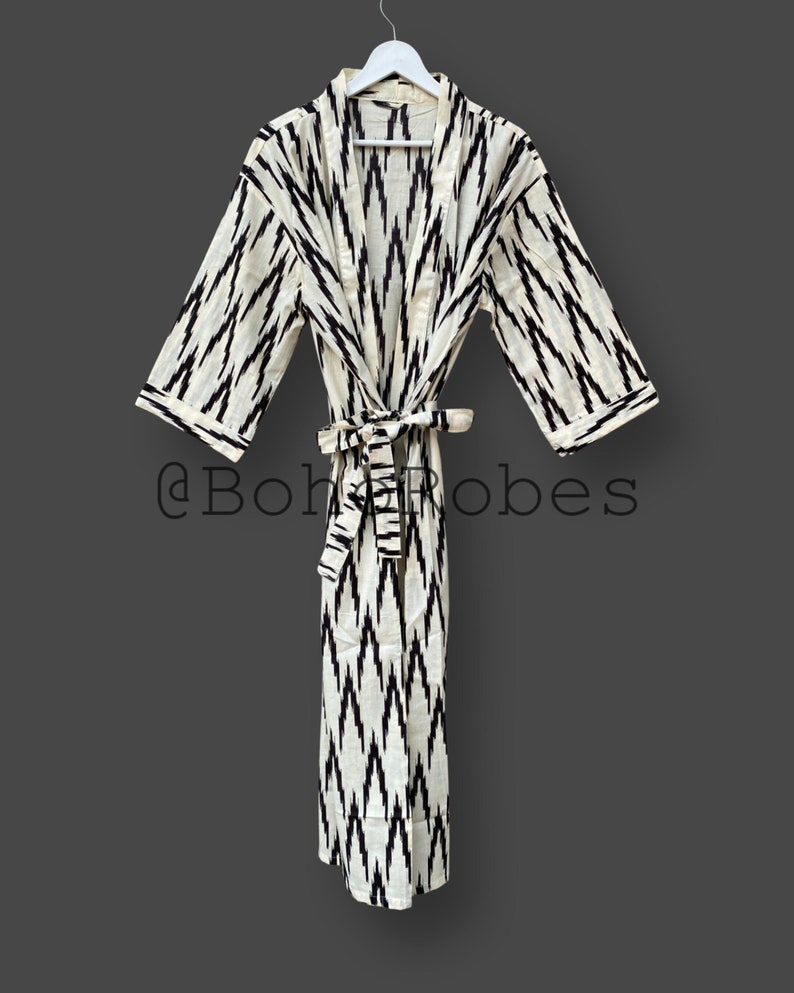 May include: A white and black ikat patterned robe with a black sash. The robe is hanging on a white hanger against a gray background. The text "@BohoRobes" is visible in the lower center of the image.