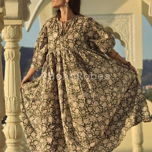 May include: A long, flowing dress featuring a floral pattern in olive green and cream. The dress has a relaxed fit, three-quarter sleeves, and a gathered waist. The text "BohoRobes" is printed on the dress.