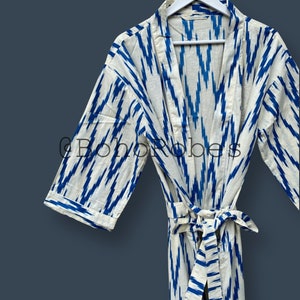 May include: A white cotton robe with a blue ikat pattern. The robe has a tie belt and long sleeves. The robe is hanging on a white hanger.