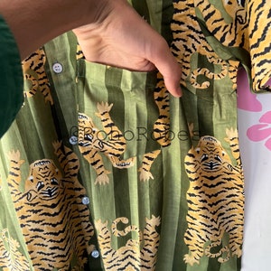 May include: A green and white striped shirt with a tiger print. The shirt has a button-up front and a pocket on the left side.
