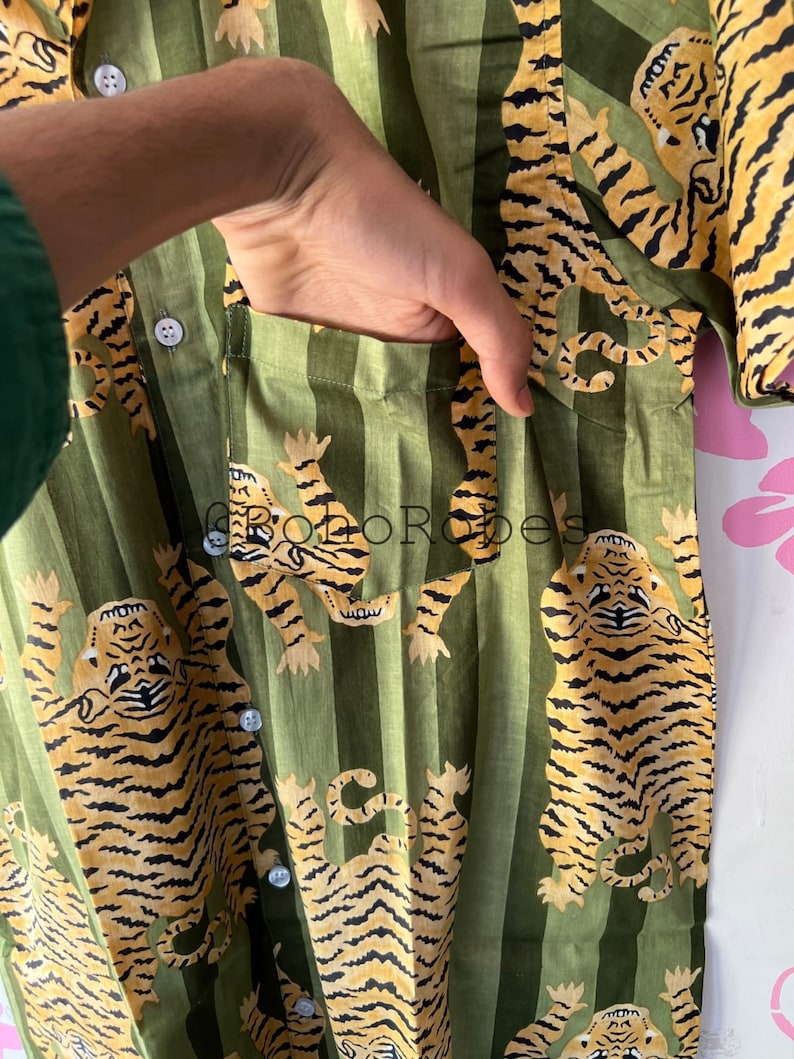 May include: A green and white striped shirt with a tiger print. The shirt has a button-up front and a pocket on the left side.