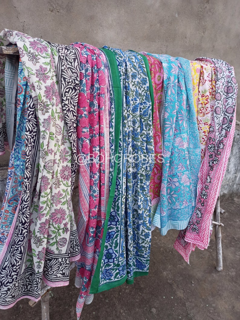 May include: A collection of colourful cotton fabrics with floral patterns. The fabrics are folded and draped over a wooden bar. The fabrics are in various shades of pink, blue, green, and yellow.