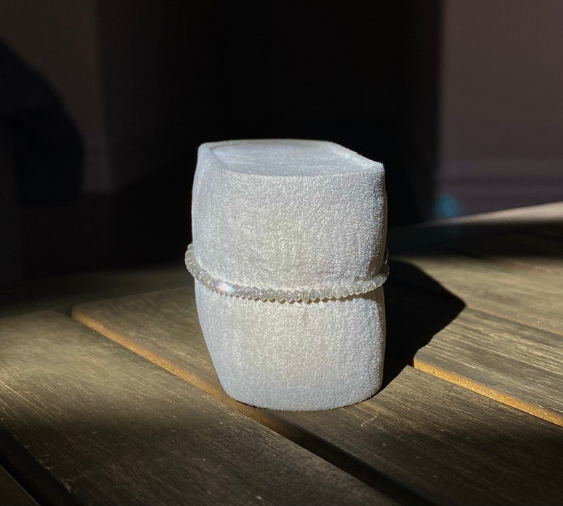 May include: A white velvet ring box with a silver beaded bracelet on top.