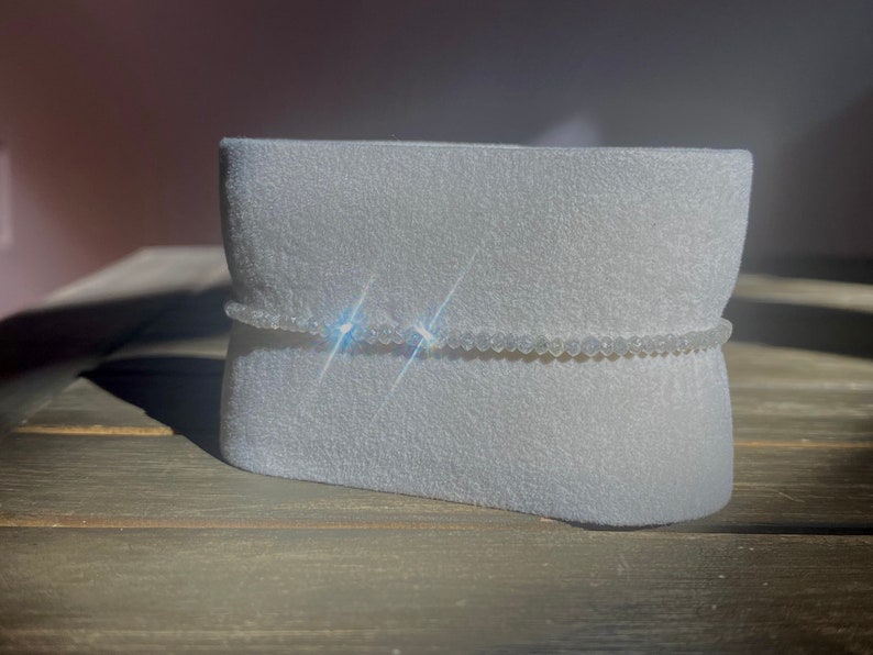 May include: A white beaded bracelet on a white foam display stand. The bracelet is made of small, round beads.