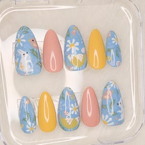 May include: A set of ten false nails with a pastel blue, yellow, and pink base. The nails are decorated with a floral pattern featuring white daisies, yellow chicks, and white bunnies.