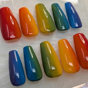 Può includere: Dieci unghie press-on con effetto ombré in colori arcobaleno. Le unghie sono disposte in due file, con i colori che passano dal rosso all'arancione, al giallo, al verde, al blu e al viola.