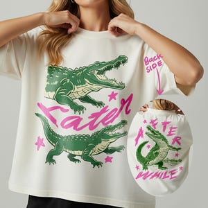 May include: Cream-colored t-shirt featuring two green alligators and the pink text "Later". The back of the shirt shows an alligator with the text "After While". The design includes pink stars.