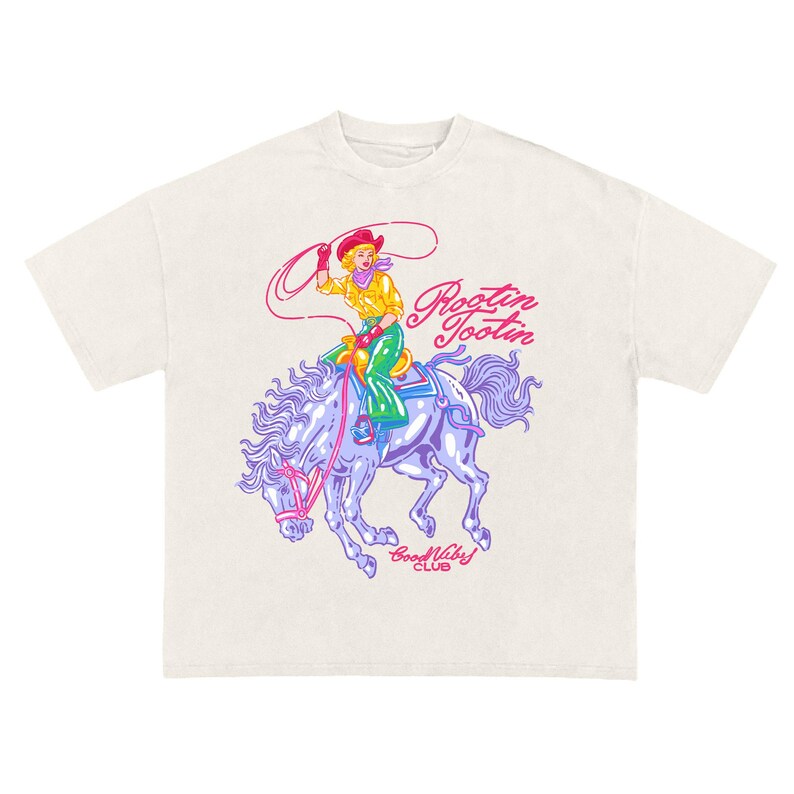 K&ouml;nnte beinhalten: Cremefarbenes T-Shirt mit einem farbenfrohen Grafikdesign einer Cowgirl auf einem Pferd mit Lasso. Der Entwurf enth&auml;lt den Text "Rootin' Tootin'" und "Good Vibes Club". Die Cowgirl tr&auml;gt einen roten Hut, ein gelbes Hemd und gr&uuml;ne Hosen.