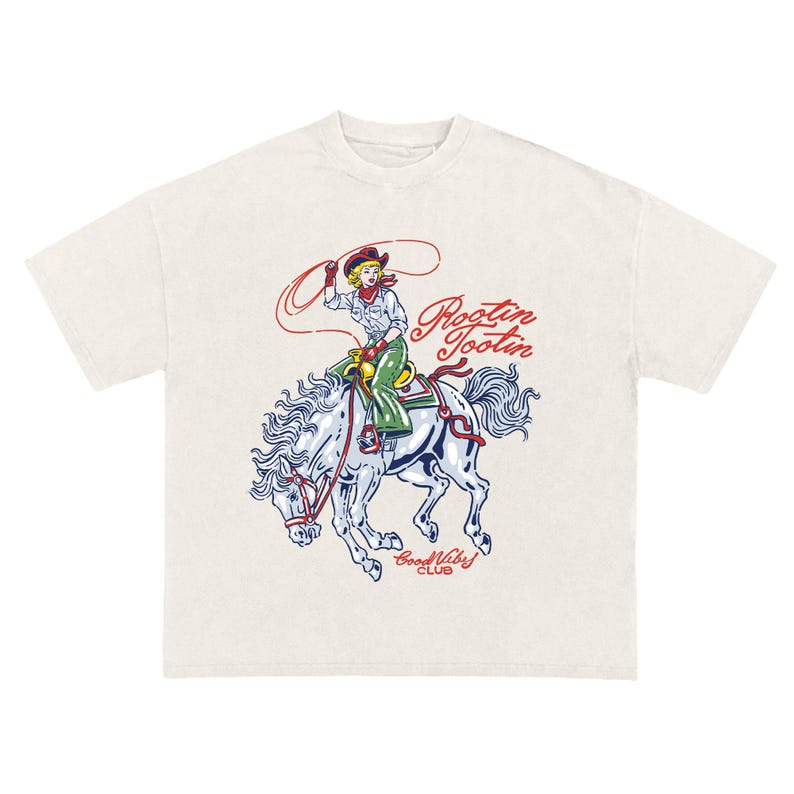 May include: Cream-colored t-shirt featuring a vintage-style illustration of a cowgirl riding a bucking horse. The cowgirl is wearing a red bandana and green pants, holding a lasso. The text "Rootin' Tootin" and "Good Vibes Club" are also on the shirt.