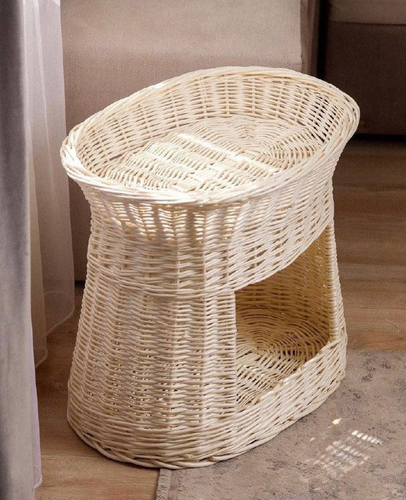 Peut inclure: Un lit pour chat en osier blanc avec une plateforme sur&eacute;lev&eacute;e et un niveau inf&eacute;rieur s&eacute;par&eacute; pour se pr&eacute;lasser. Le lit est de forme ovale et pr&eacute;sente un design tiss&eacute;.