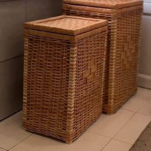 Puede incluir: Dos cestos rectangulares de mimbre para la colada con tapas. Las cestas están tejidas en color marrón claro, con forma rectangular y un patrón tejido. Las cestas son de diferentes tamaños y están colocadas una al lado de la otra.