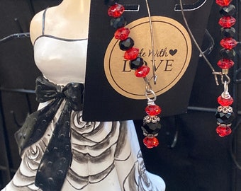 Puede incluir: Un par de pendientes colgantes con cuentas negras y rojas. Los pendientes cuelgan de un maniquí blanco que lleva un vestido blanco y negro. La etiqueta del maniquí dice "Made With Love".