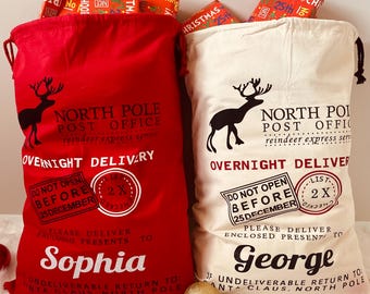 May include: Two Christmas gift sacks, one red and one cream-colored, with black reindeer silhouettes and text. The red sack says "Sophia" and the cream sack says "George". Both sacks have "North Pole Post Office" and "Overnight Delivery" printed on them.