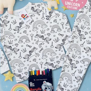 May include: White pajama set with a black unicorn, rainbow, and crown pattern. Includes a set of acrylic markers and plush unicorn toys. The text "COLOUR ME IN UNICORN EDITION!" is visible.