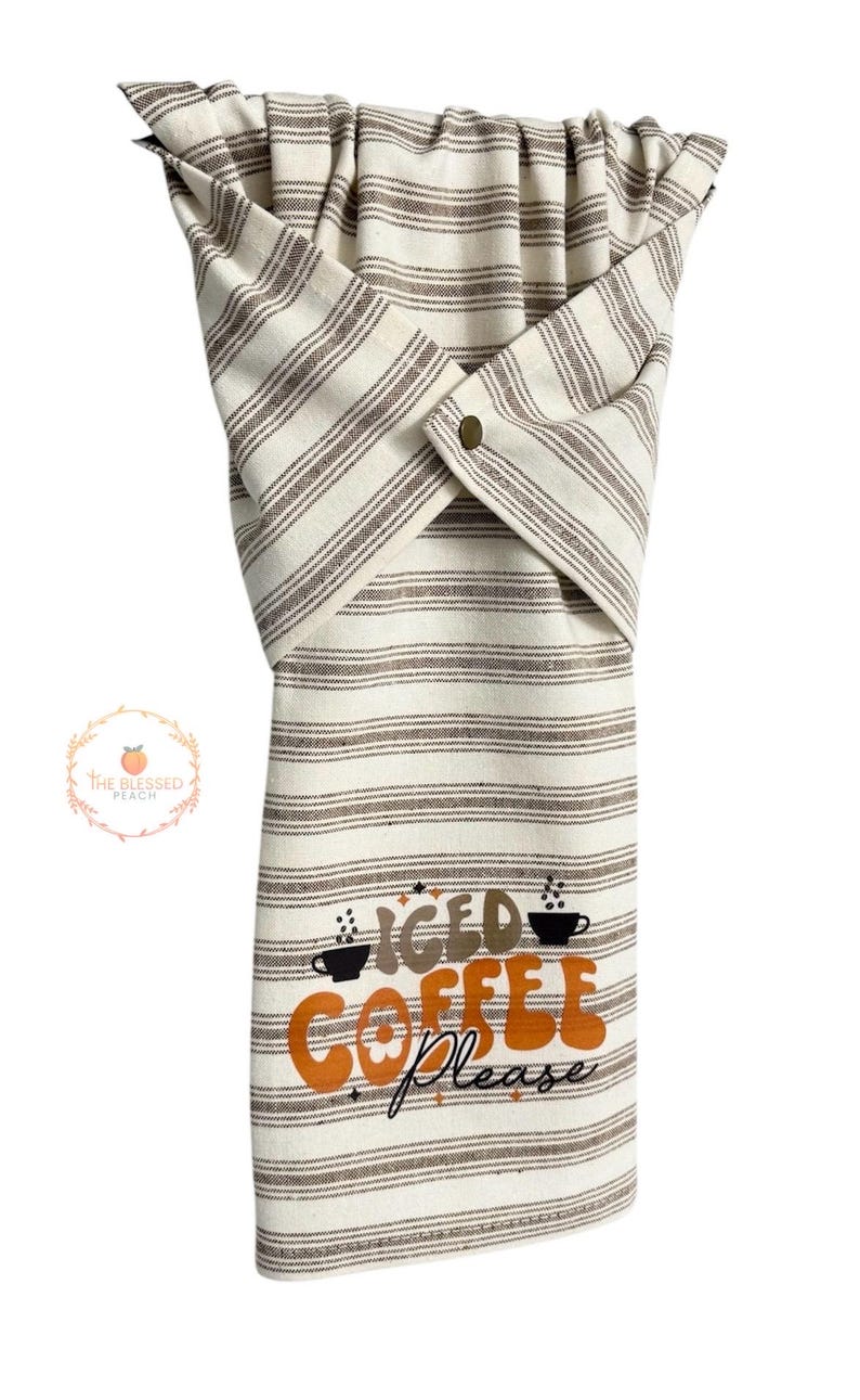 One stay put kitchen towel with brown stripes on an ivory background. The towel has the text 'Iced Coffee Please' printed on the front of the towel in orange and brown lettering with a black coffee cup on each side of the text. The towel has a snap closure so it can stay in place on an oven/stove/dishwasher handle. This listing is for one towel and includes free shipping.
