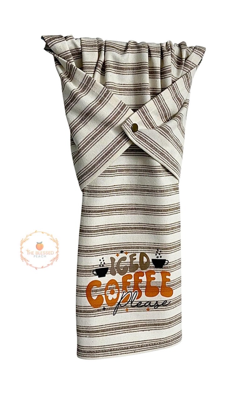 One stay put kitchen towel with brown stripes on an ivory background. The towel has the text 'Iced Coffee Please' printed on the front of the towel in orange and brown lettering with a black coffee cup on each side of the text. The towel has a snap closure so it can stay in place on an oven/stove/dishwasher handle. This listing is for one towel and includes free shipping.